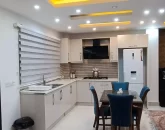 کابینت های سفید و میز غذاخوری و سقف نورپردازی شده با نور زرد آشپزخانه ویلا در سرخرود
